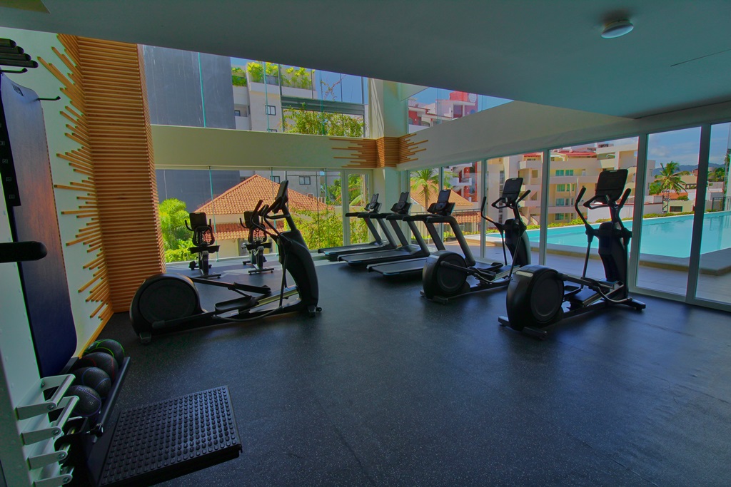 Gym with view to pool area and common area, with gym equipment, four trendmills. lifts, weights.