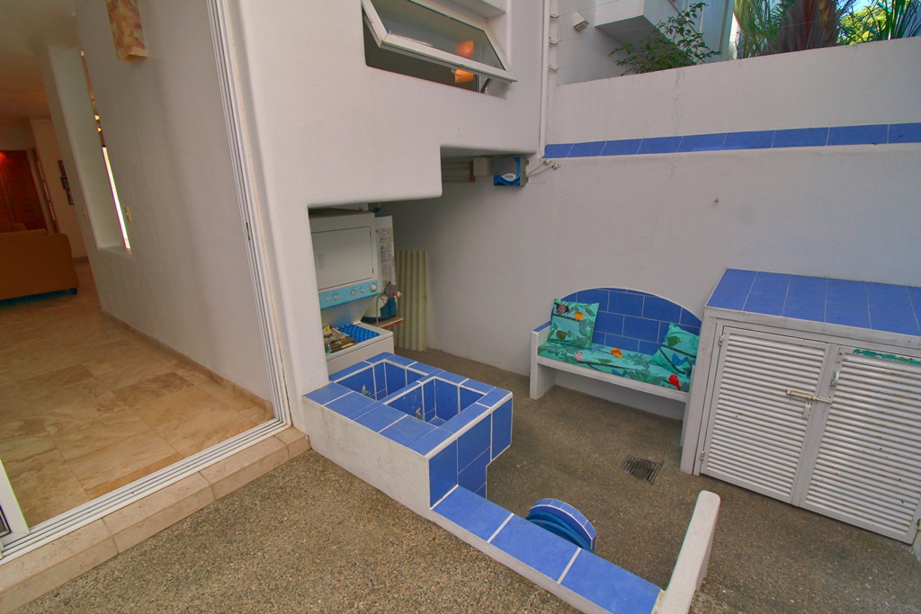 Laundry area, sink with blue tiles. bench, stack able washer and drier.