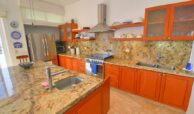 Brown color granite counter top kitchen, wood and glass upper and lower cabinets, oven, stove, hood, fridge.