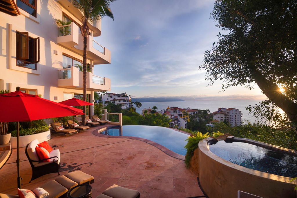 Panoramic view from Villa Divina where you can see pool, a jacuzzy, building facing the ocean, with a sunset in the background.